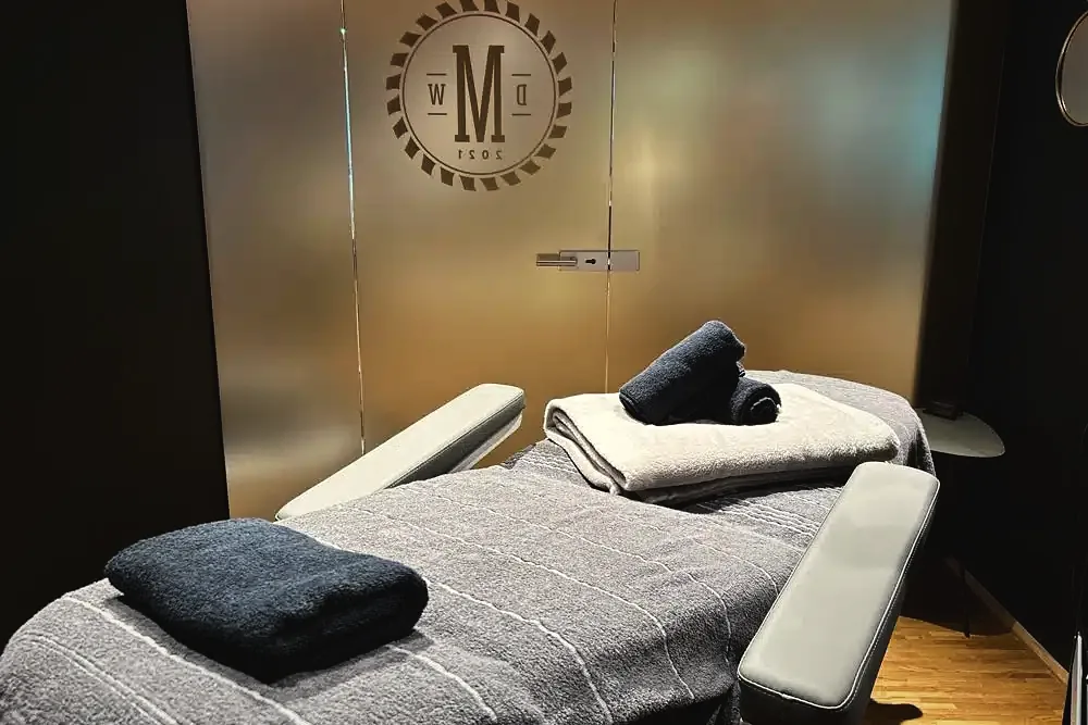 Behandlungsliege mit Handtüchern im Waxing-Raum der Männer Werkstatt vor der Glastür mit Werkstatt-Siegel