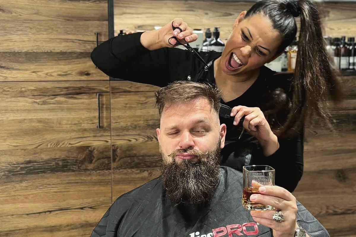 Probelauf für Frisur und Bart vor der Hochzeit: Friseurin schneidet einem Gast mit langem Bart die Haare