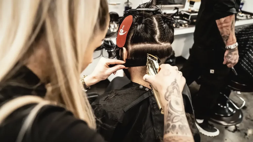 Bräutigam-Frisur: Friseurin schneidet einem Kunden die Haare im Nacken mit der Haarschneidemaschine