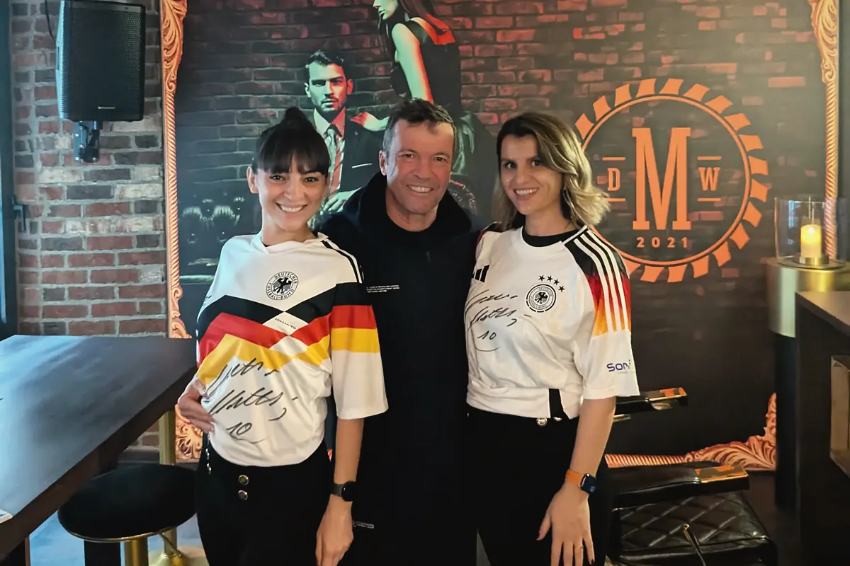 Weltmeister-Variante: Zwei Mitarbeiterinnen der Männer Werkstatt in signierten Deutschland-Trikots mit Lothar Matthäus