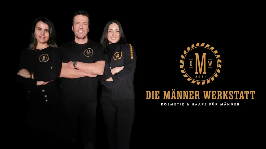 Lothar Matthäus mit zwei Mitarbeiterinnen der Männer Werkstatt vor dem Werkstatt-Logo